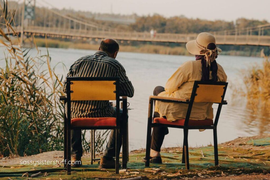 older couple relax on the shore of a river overlooking an old bridge as they find calm, presence, and focus.