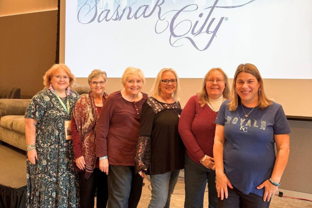 six women who went on a girls' weekend getaway together pose in front of a presentation board.