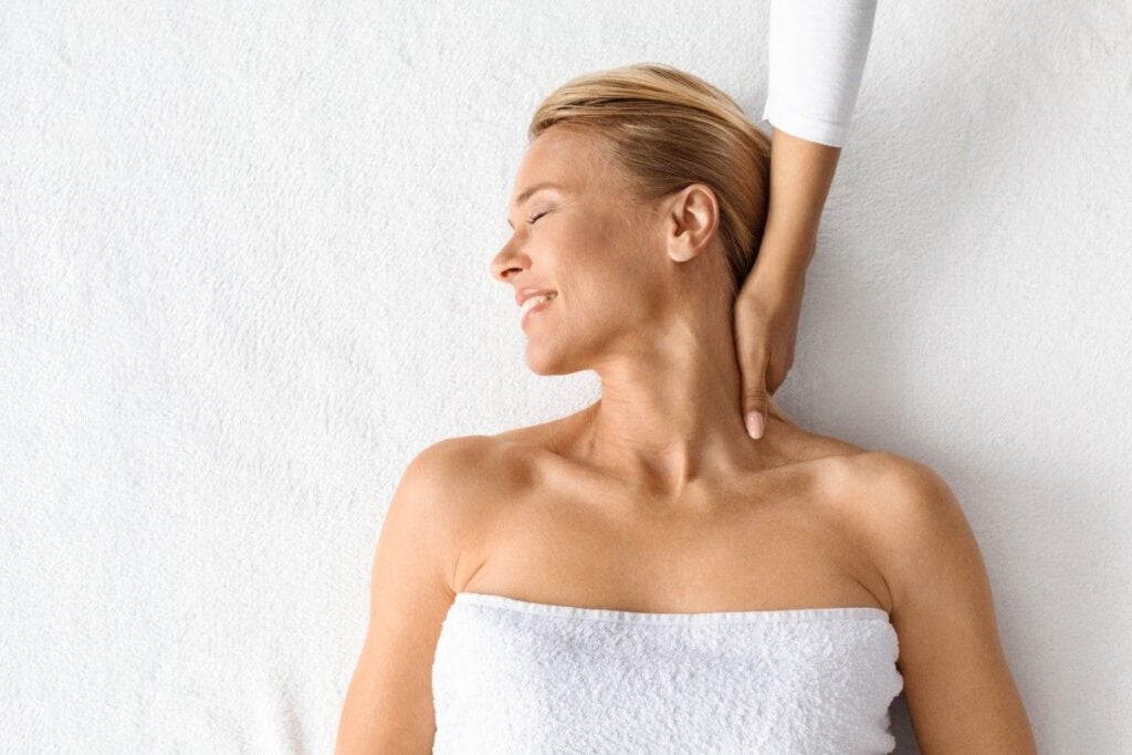 blonde haired woman lays on her back and gets a neck massage.