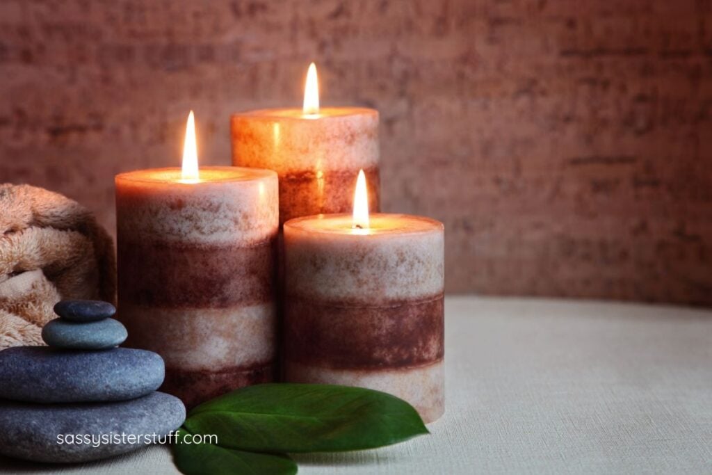 close-up of three lit candles, balanced rocks, two leaves, and a towel.