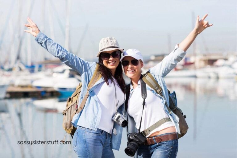two happy midlife women pose with their arms outreached while traveling.