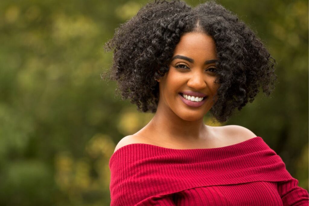 beautiful black woman in a red sweater smiling after reading her affirmations for confidence in the new year.