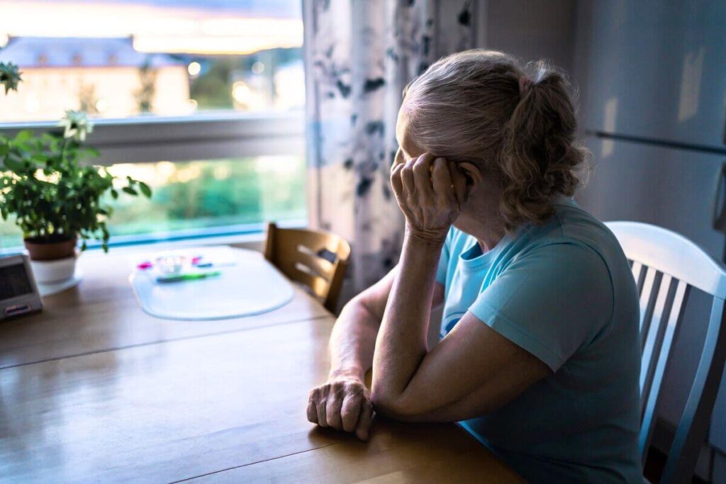 midlife woman sitting at a kitchen table looking out the window trying to figure out how to tame your anxiety over the unknown.