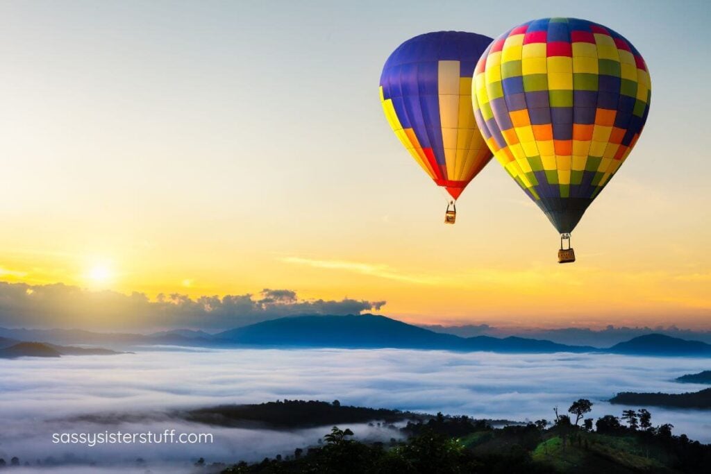 two hot air balloons with the sun setting in the background.