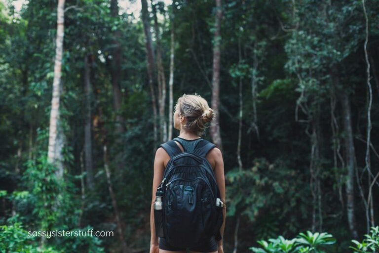 a woman with a backpack pausing to look into the forest where she is going to hike.