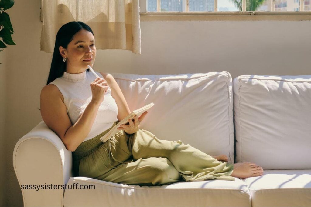 midlife Asian woman sits on the sofa and her favorite mindfulness quotes in her journal.