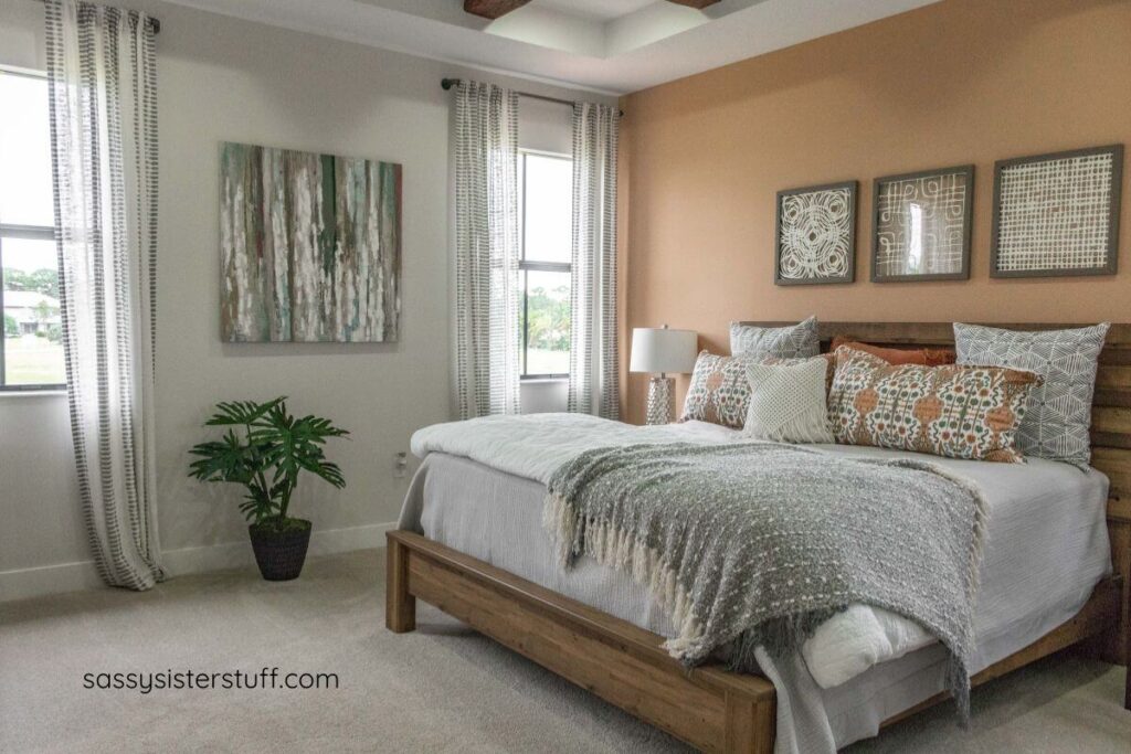 a bedroom with an accent wall painted in a calming peach color and bed accessories in shades of peach, white, and gray.