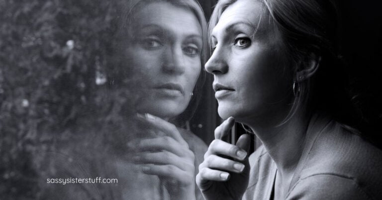 midlife woman and her reflection as she looks out the window into a rainy night.