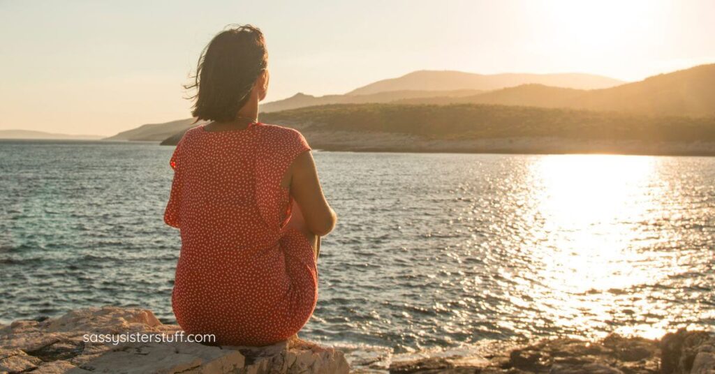 midlife woman sitting on the edge of a lake reflecting about her life.