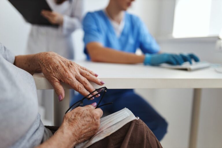 Older woman at the drs, showing her hands and dr in the background