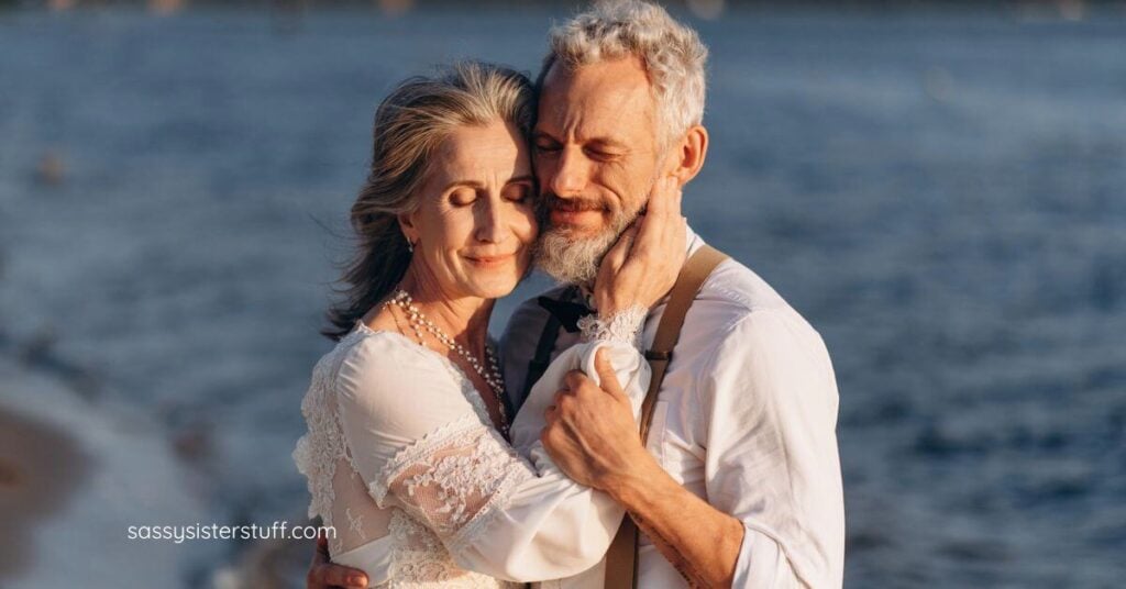 older bride and groom hugging cheek to cheek on the beach.