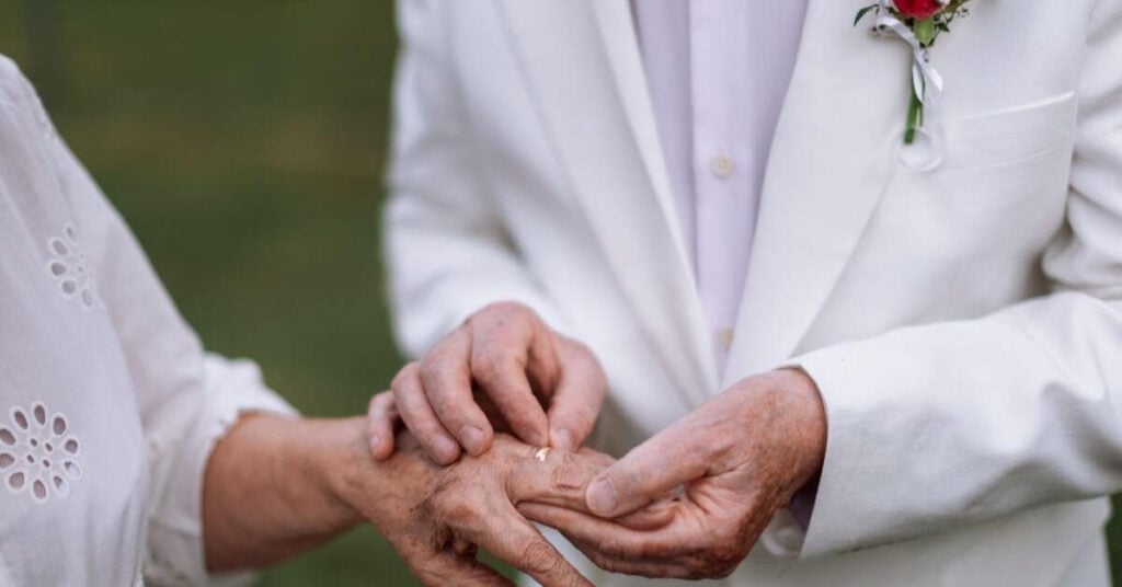 older groom putting a ring on his older bride's finger during their second wedding later in life.