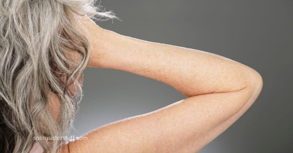 back view of woman running her hand through her shoulder length gray curly hair.