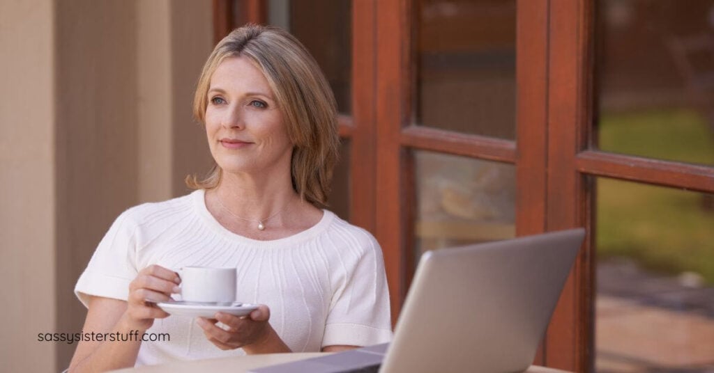 a midlife woman with a cup of tea sits outside at a cafe table pondering the power of reflection and finding her north star.