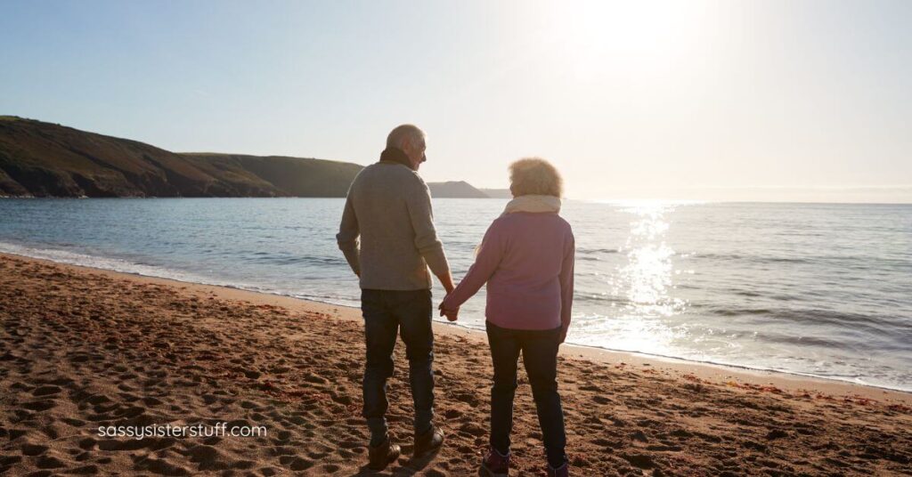 Married middle aged couple happily walk on the beach hand-in-hand after using tips for downsizing and reorganizing after the kids move out. and gaining clarity in their lives.