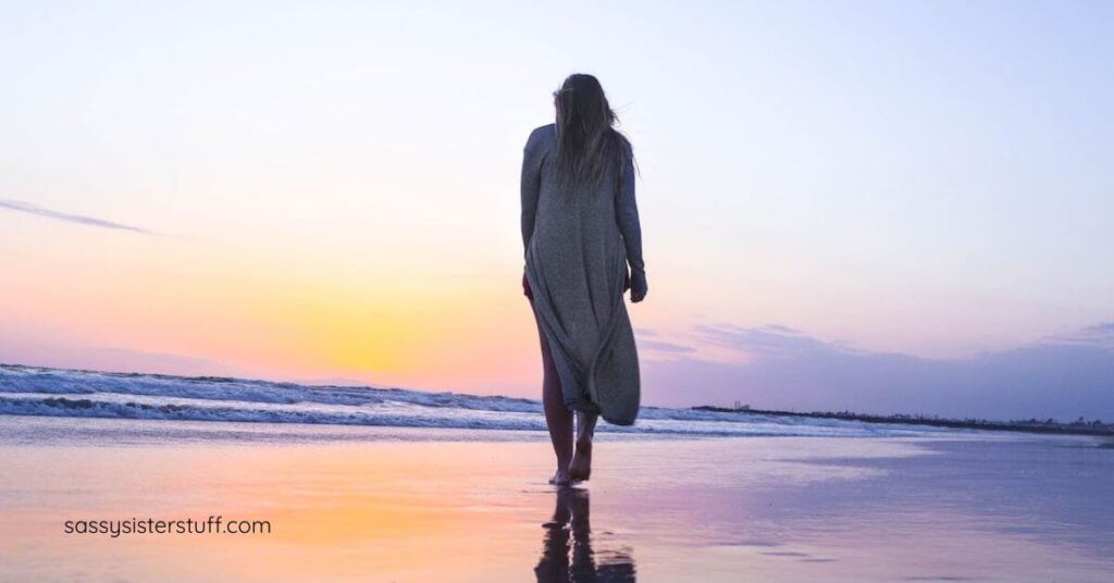 woman with menopause brain fog walks barefooted along a beach in a beautiful sunset.