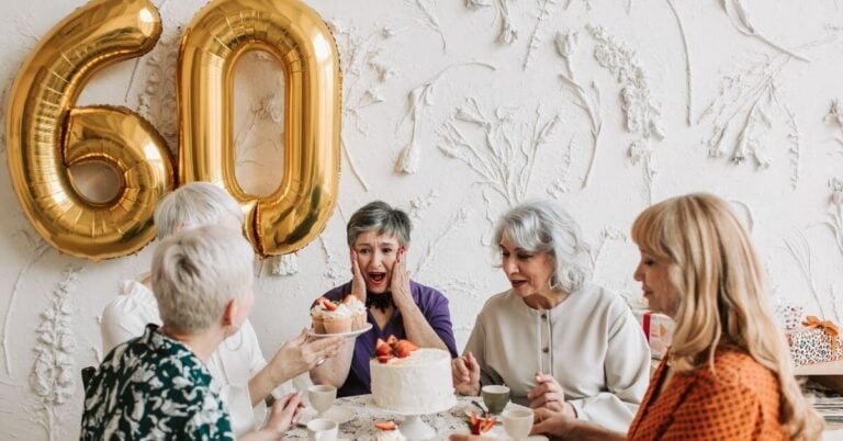 five ladies celebrate a friends 60th birthday with a cake and a large gold 60 balloon.
