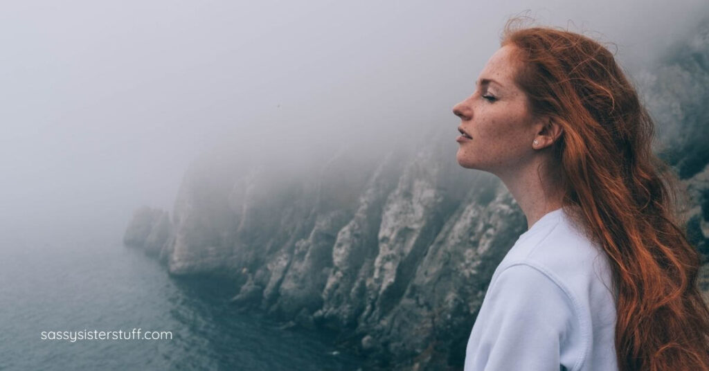 midlife woman standing on a cliff in the fog with her eyes closed thinking about menopause brain fog.