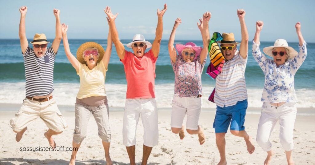 six elderly people happily jump up for a picture on the beach.