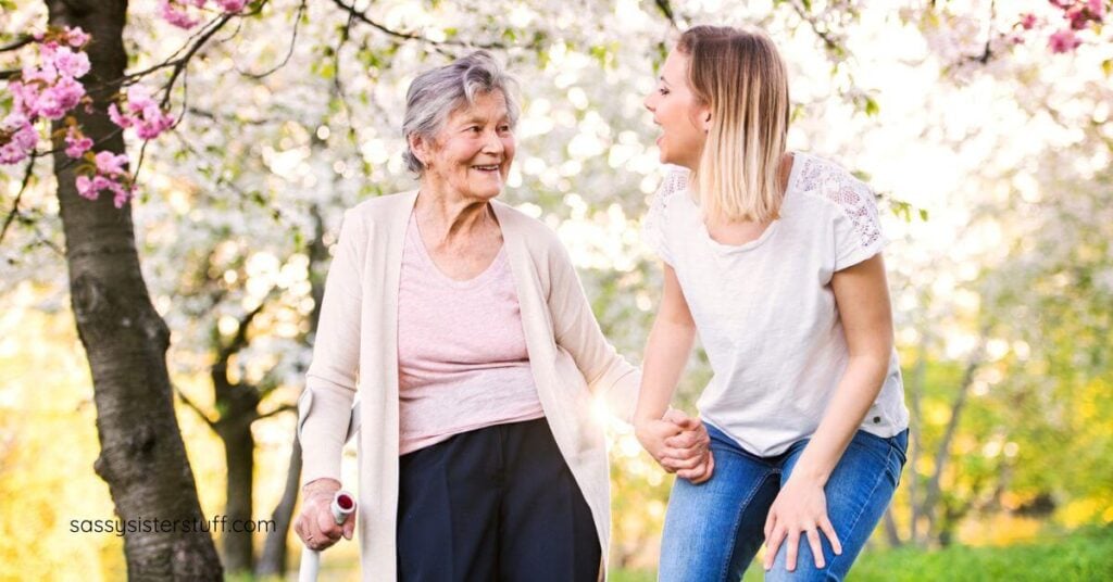 an elderly mother and adult daughter take a walk in a park.