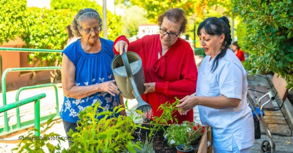 two elderly women and a nurse work in a garden together.