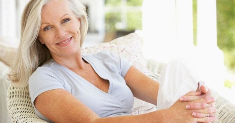 middle age blonde woman relaxing on a patio smiling for the camera.