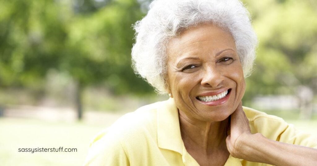 middle aged Black woman smiling for the camera as she sits outside in a park.