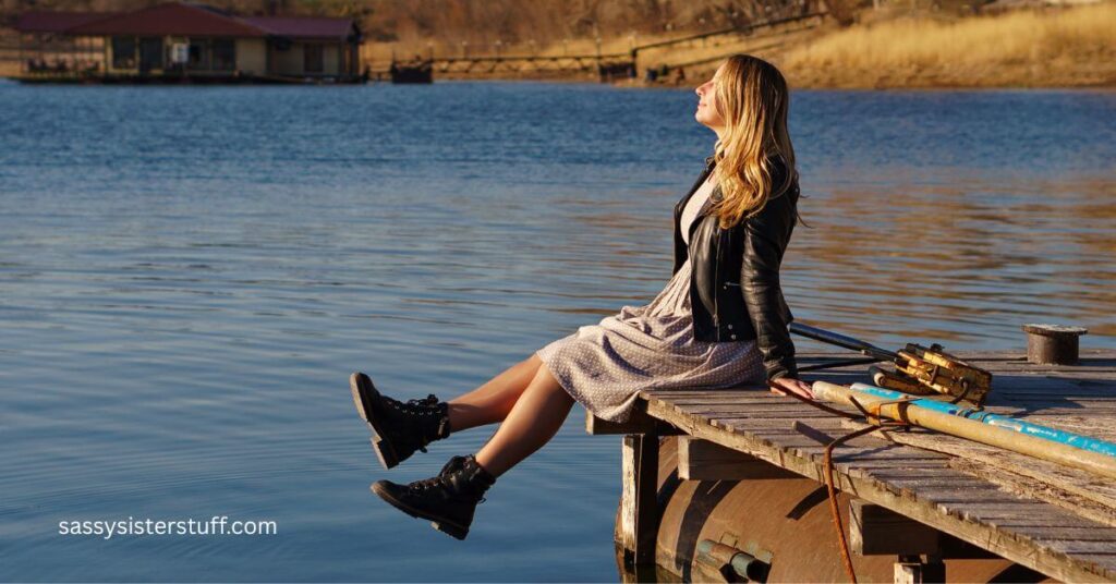 midlife woman who is practicing 30 things to do to feel like yourself again as she sits on the end of a pier looking into the sky.