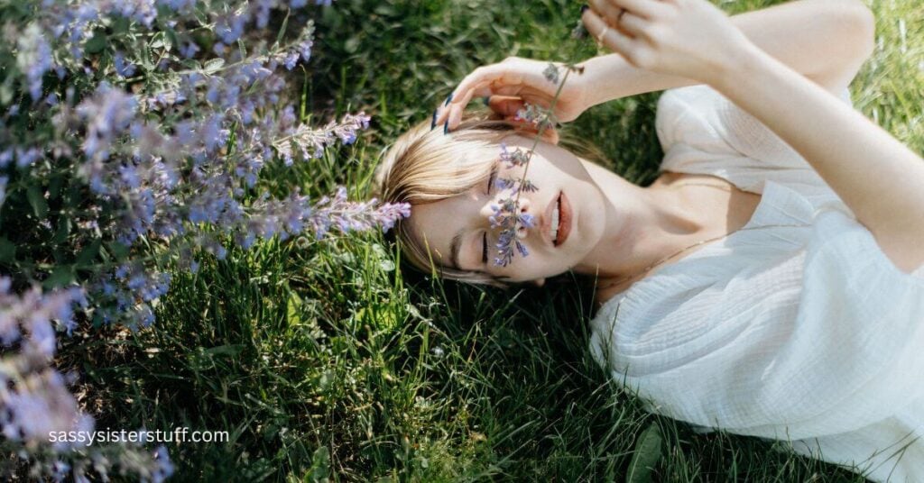 woman is laying on the ground smelling a lavender flower as part of 30 things to do to feel like yourself again.