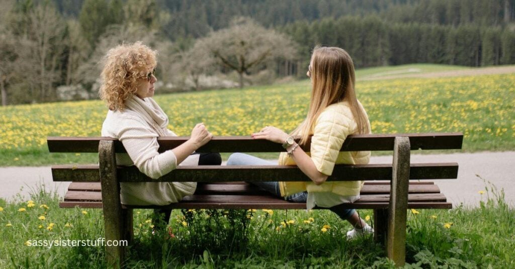 two women sitting on a bench talking looking over a beautiful park.
