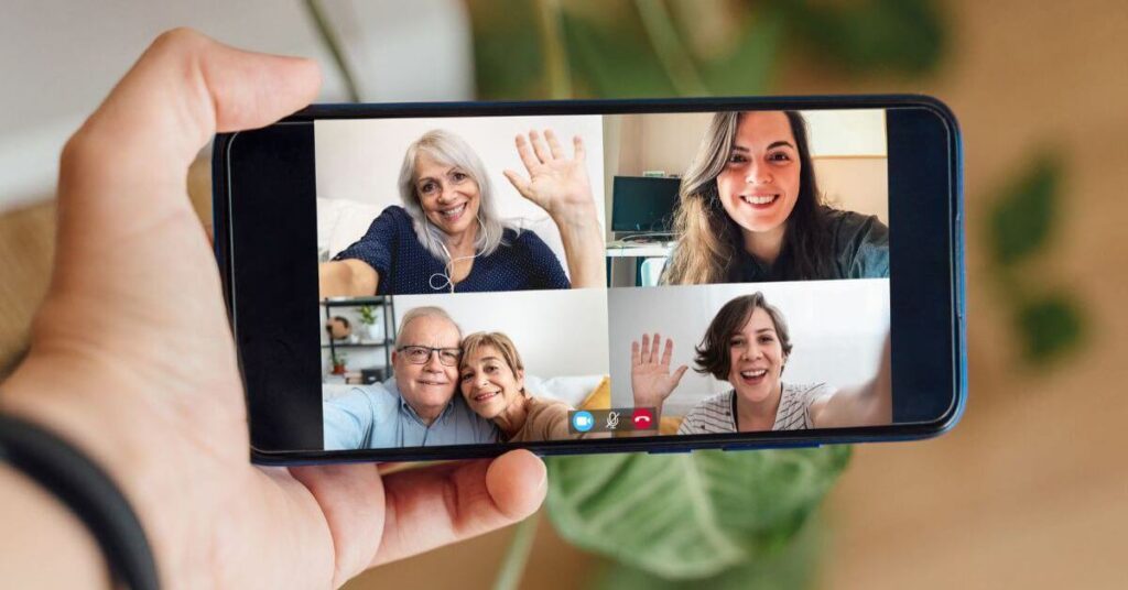 closeup of a hand holding a phone that has a Zoom image with four pictures of family members connecting across the miles.