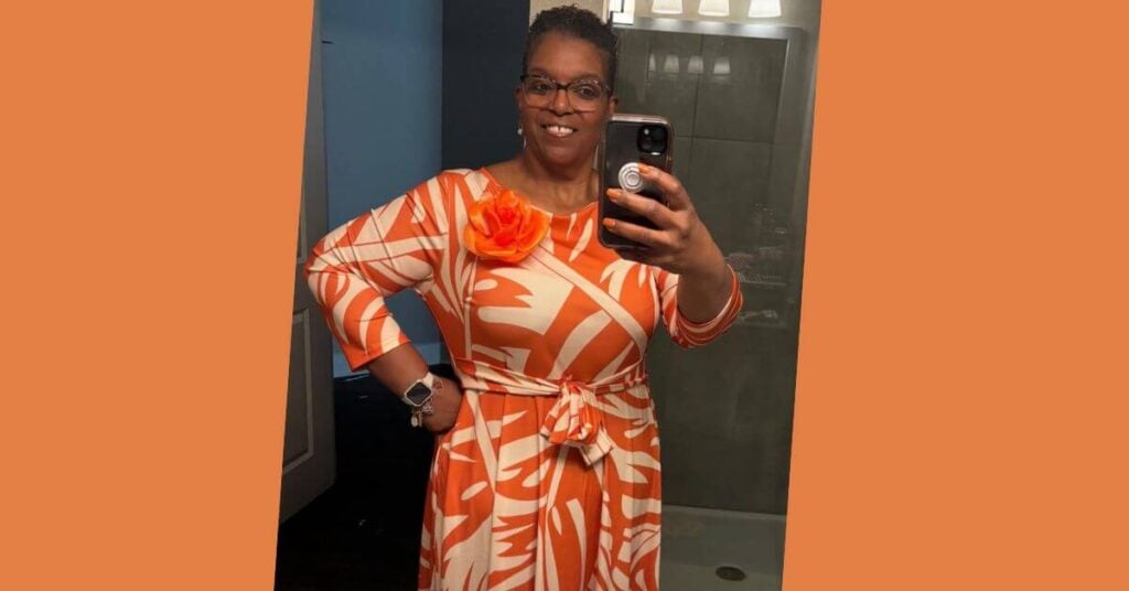 Beautiful Black woman takes a selfie in the mirror wearing a bright orange dress.