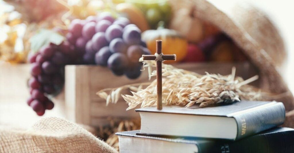 a stack of books with grapes and other fruits on top with a small decorative cross.