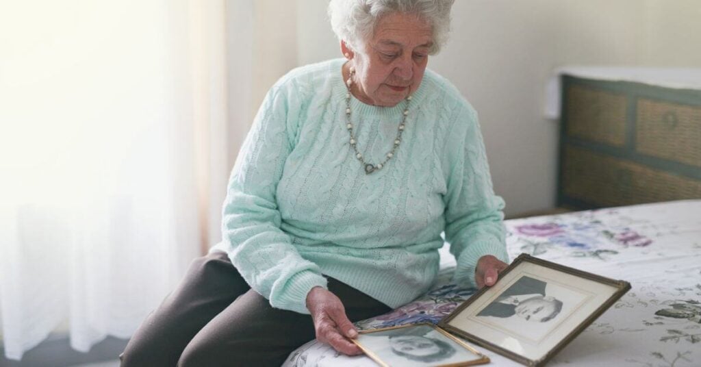 an elderly woman looking at old family photos, navigating the emotional weight of family heirlooms.