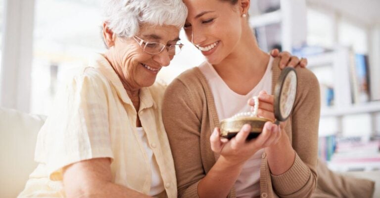 elderly mother and adult daughter hug check to check as the mother passes on family heirloom pearls.