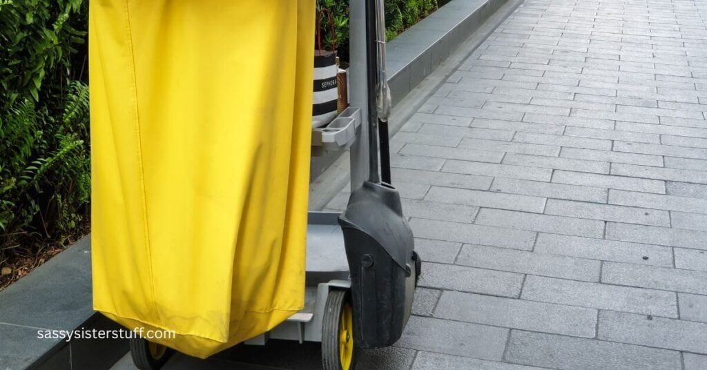 outdoor cleaning supply cart on a sidewalk next to a hedge.