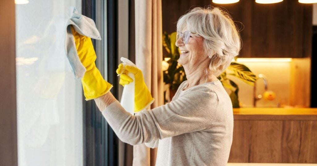 midlife woman happily cleans a window in her home.