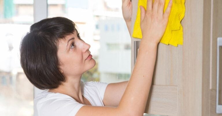 midlife woman cleans a cabinet door in her house.