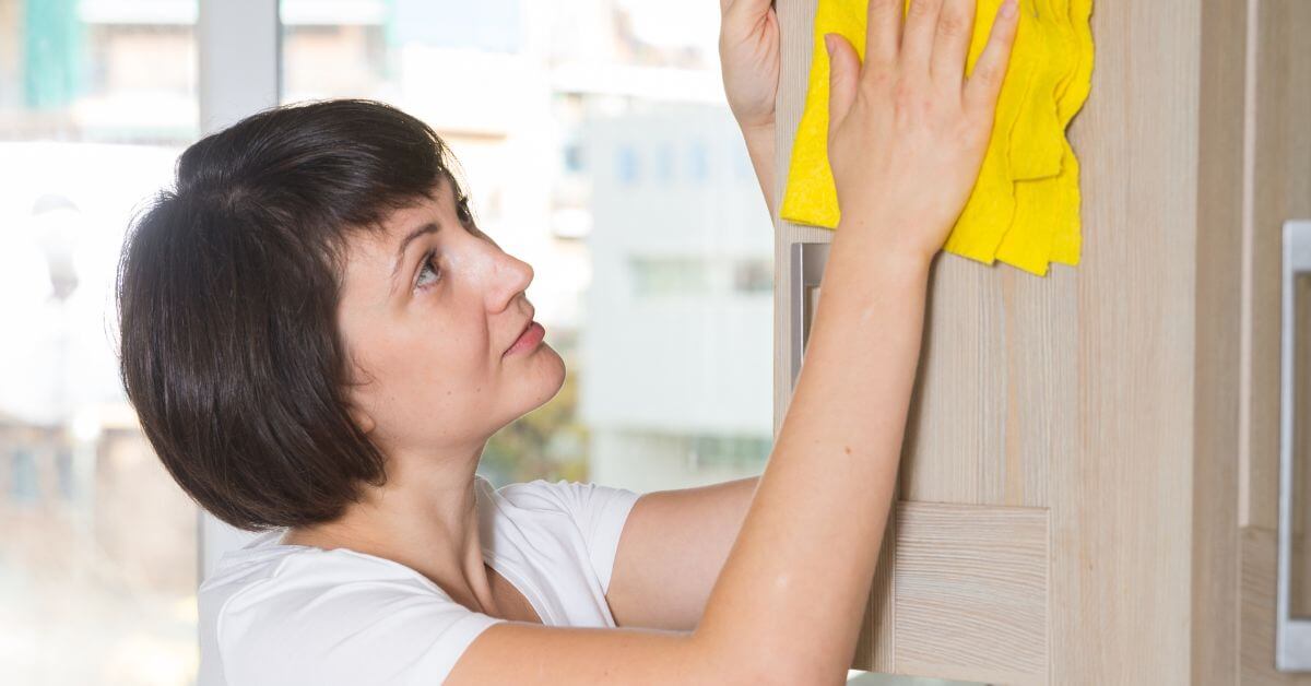midlife woman cleans a cabinet door in her house.