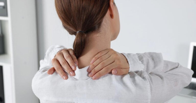 woman with severe neck pain rubs her neck and considers the biopsychosocial approach to pain management.