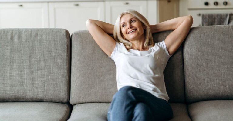a midlife woman has accepted living alone again and relaxes on her sofa.