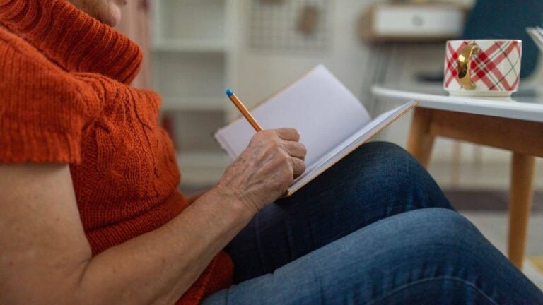 close up of woman sitting on her floor writing in her journal.