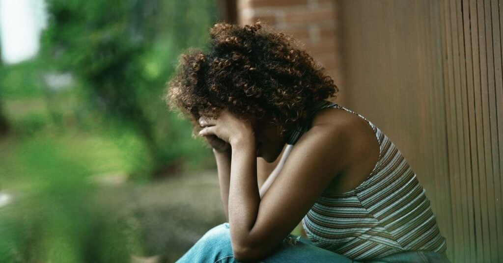 very sad woman sits outside with her head between her hands in grief.