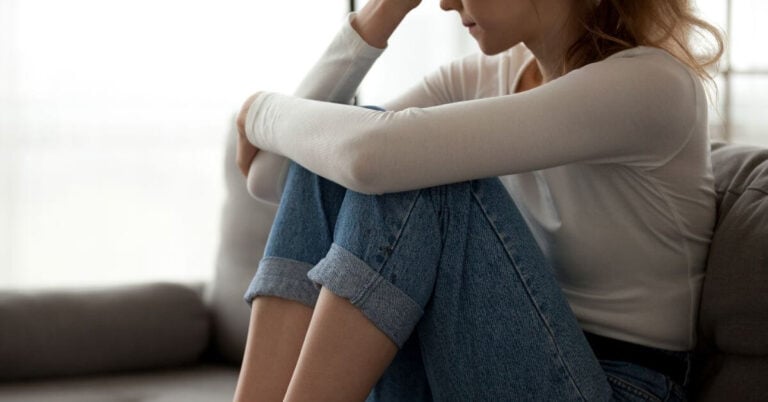 very sad woman sitting on her sofa with her knees pulled up and her head down in grief.