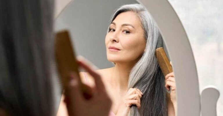 beautiful midlife woman combs her long gray hair carefully after learning how menopause changes hair.