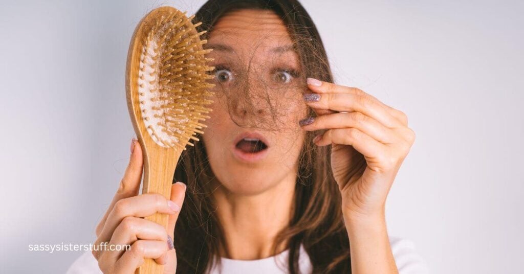 midlife woman pulls hair out of her brush and looks shocked.