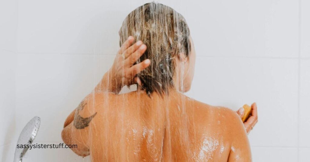 the back of a woman in the shower shampooing her hair.