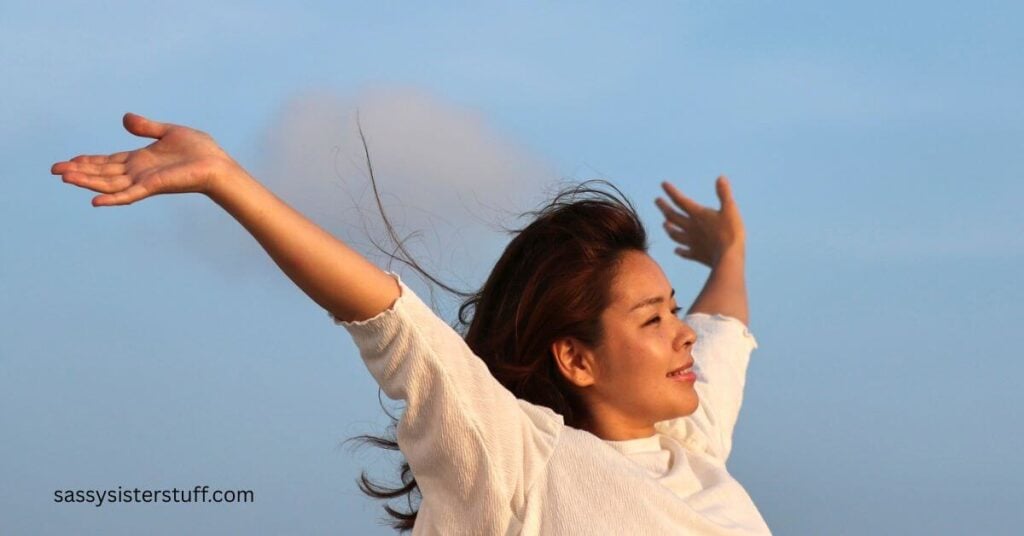 midlife woman happily throws her hands up in the air to release worry and show she knows how to strength your faith.