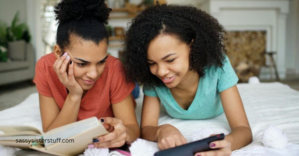 two young ladies laying on a bed reading together comfortably.