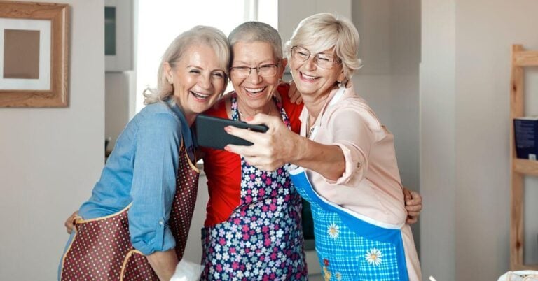 three midlife women taking a selfie together as they gather in one of their homes.